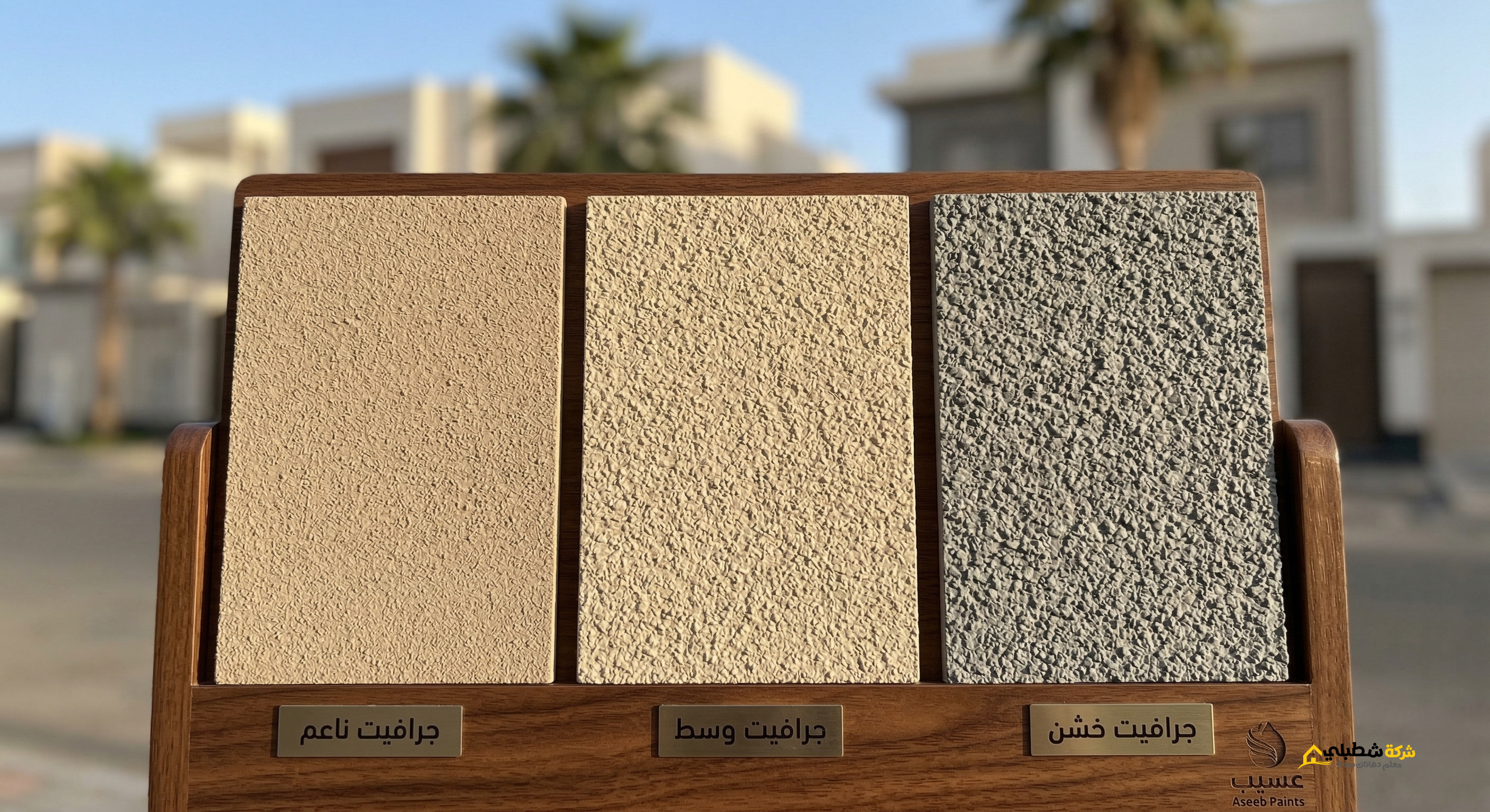 الصورة بزاوية مقربة جداً لإظهار عمق الحبيبات بدقة، وتسمية كل عينة باللغة العربية (جرافيت ناعم، جرافيت وسط، جرافيت خشن) كما هو مطلوب. الخلفية ضبابية تظهر فيلا سكنية في جدة تحت سماء زرقاء مشمشة لتعزيز سياق المقال.